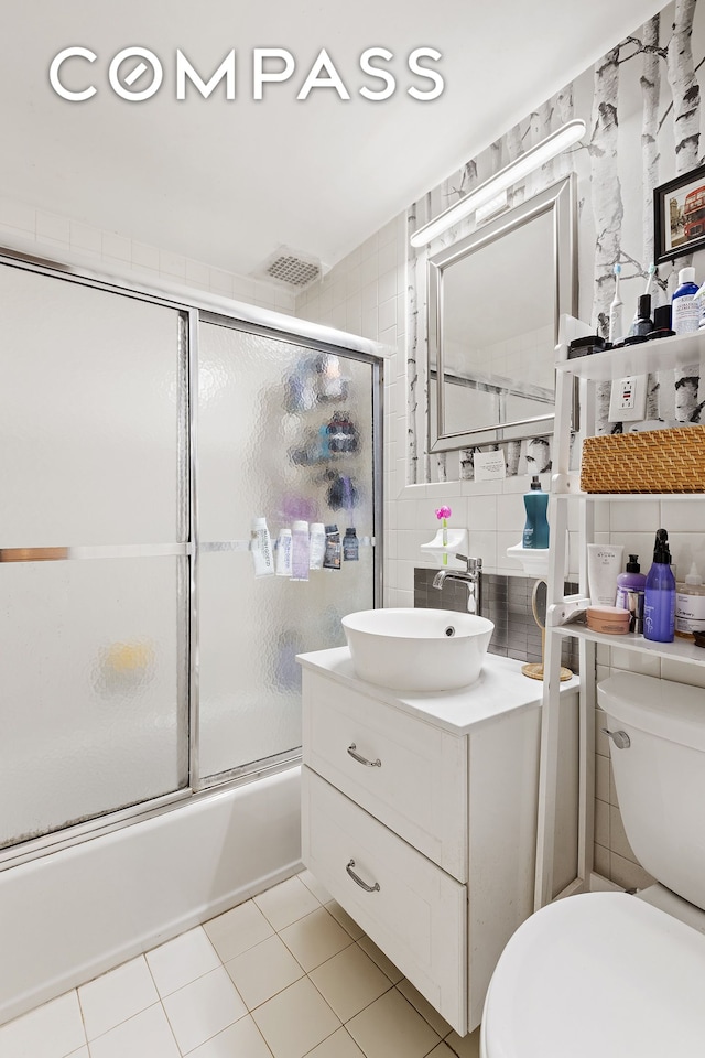 138 W 73rd St, New York City, NY 10023 - full bathroom featuring tile walls, toilet, tile patterned floors, vanity, and bath / shower combo with glass door