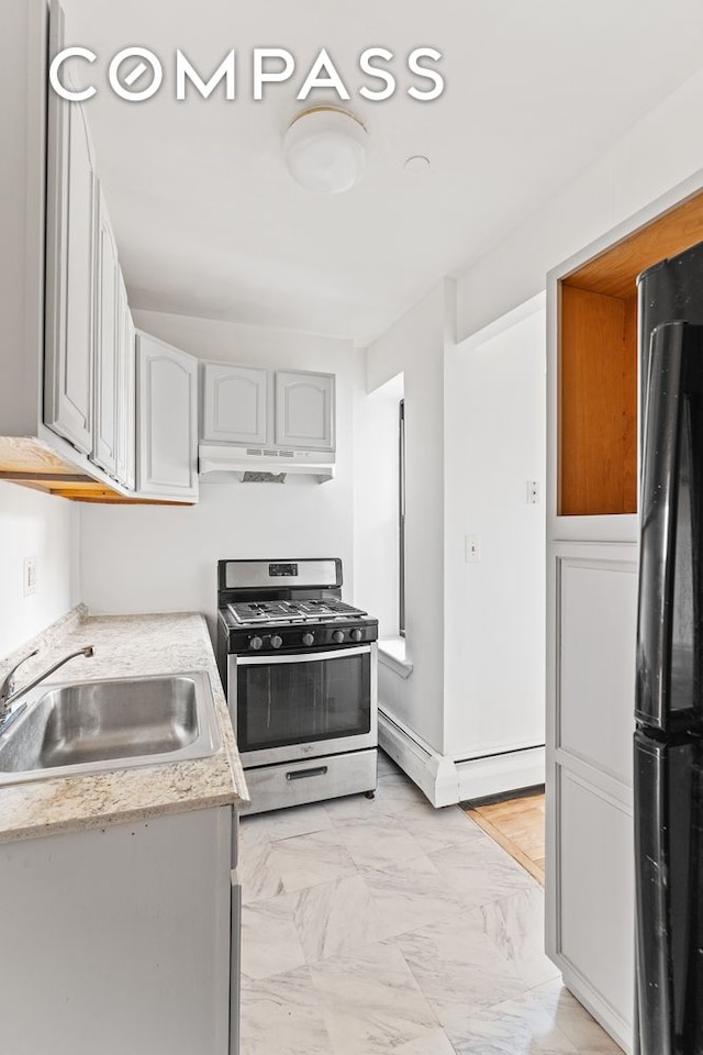 kitchen with stainless steel range with gas cooktop, a sink, freestanding refrigerator, under cabinet range hood, and light marble finish floors