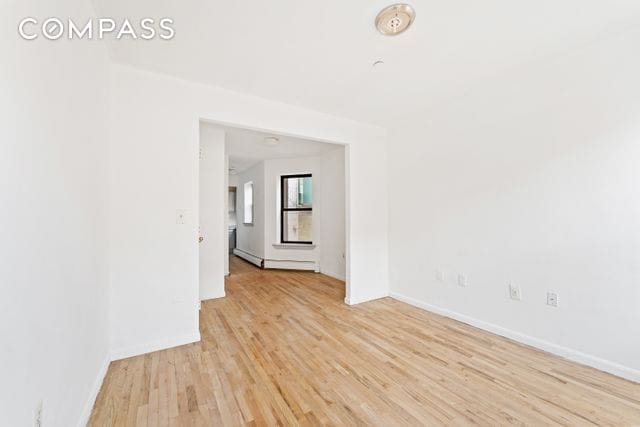 unfurnished room featuring light wood-style floors, a baseboard heating unit, baseboards, and a smoke detector