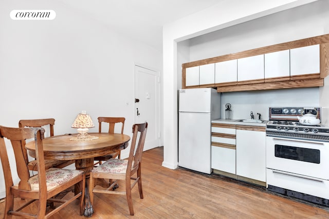kitchen with white appliances, light wood finished floors, white cabinetry, light countertops, and a sink