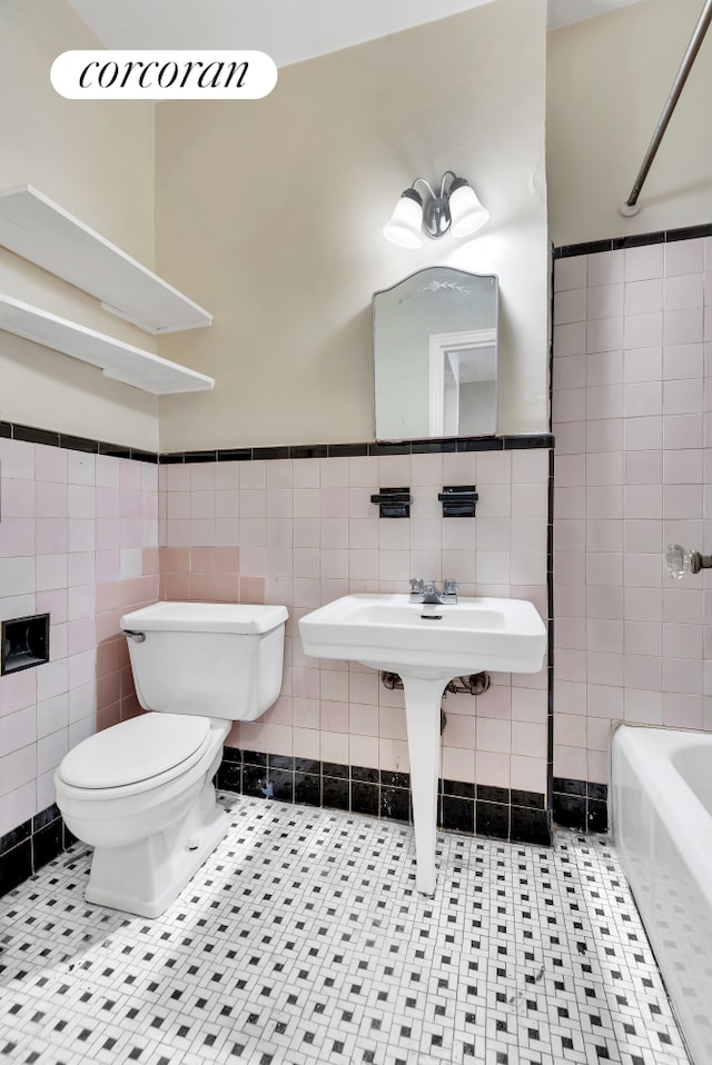 full bath with tile walls, a tub to relax in, toilet, tile patterned floors, and a wainscoted wall