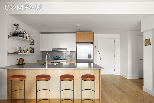 kitchen with stainless steel fridge, a sink, under cabinet range hood, a kitchen bar, and a peninsula