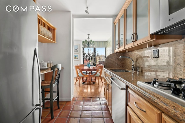 kitchen with appliances with stainless steel finishes, a sink, tasteful backsplash, glass insert cabinets, and a chandelier