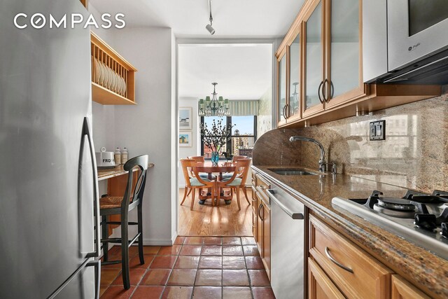 1199 Park Ave Unit 10K, New York City, NY 10128 - kitchen with stainless steel appliances, a sink, backsplash, glass insert cabinets, and a chandelier
