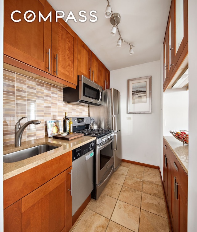 88 Bleecker St Unit 6C, New York City, NY 10012 - kitchen with appliances with stainless steel finishes, decorative backsplash, brown cabinets, light stone countertops, and light tile patterned floors
