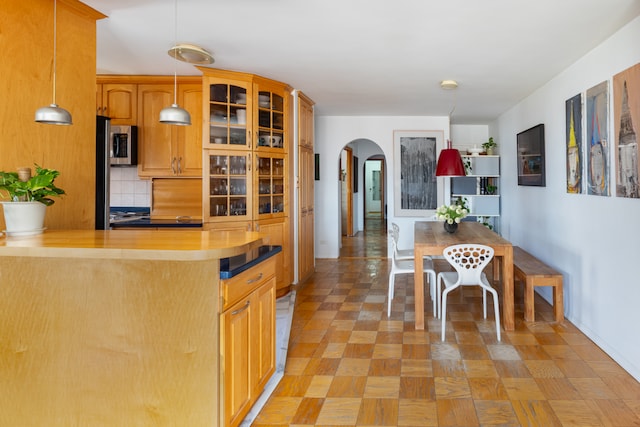 kitchen featuring arched walkways, stainless steel microwave, glass insert cabinets, decorative light fixtures, and decorative backsplash