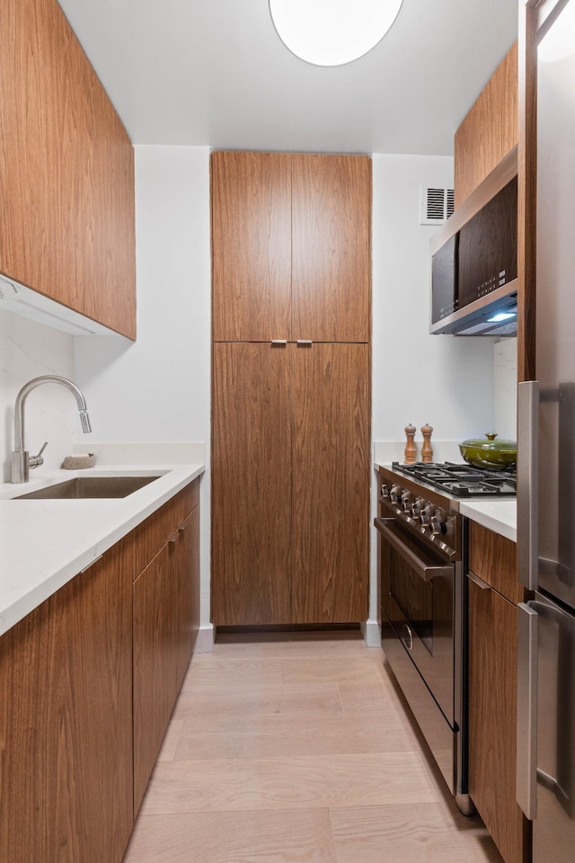 kitchen featuring appliances with stainless steel finishes, a sink, light countertops, modern cabinets, and brown cabinets