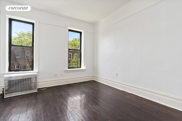 spare room featuring wood-type flooring, baseboards, and radiator heating unit