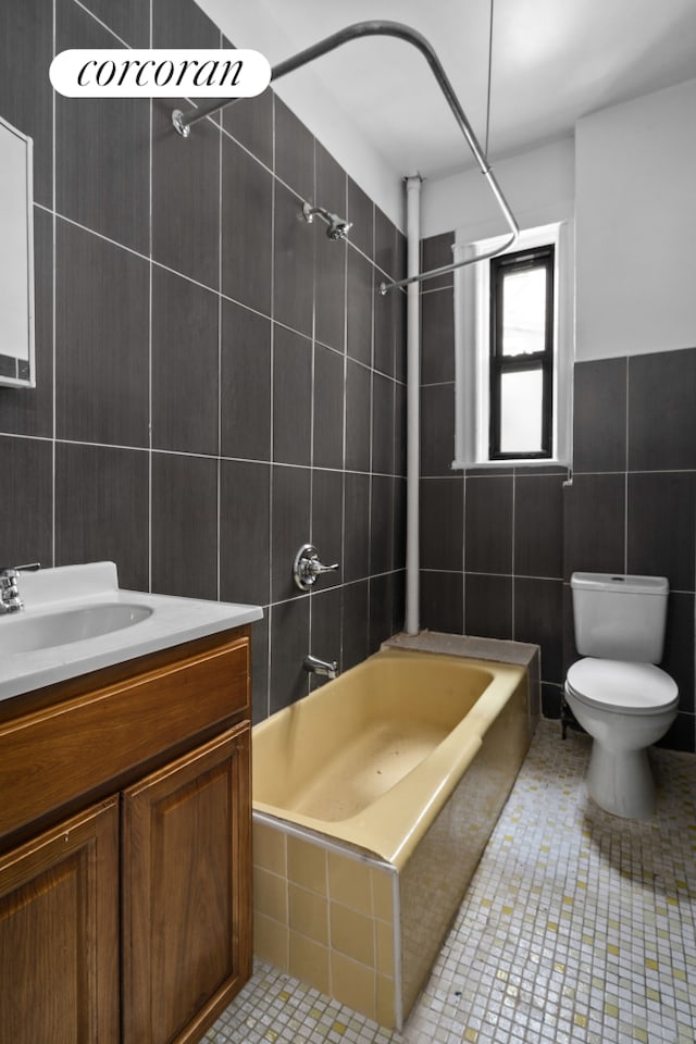bathroom with tile walls, bathing tub / shower combination, toilet, vanity, and tile patterned flooring