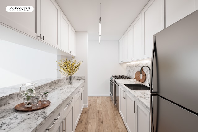 kitchen featuring freestanding refrigerator, stainless steel gas range, a sink, white cabinetry, and light wood finished floors