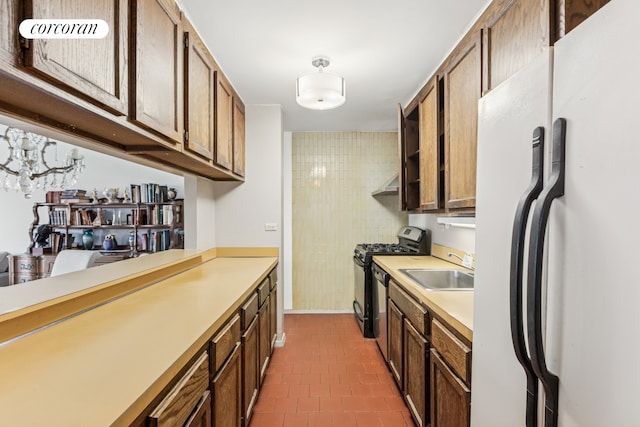 kitchen featuring freestanding refrigerator, black gas stove, light countertops, dark tile patterned flooring, and a sink