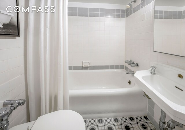 full bath featuring tile walls, shower / tub combo, toilet, and a sink