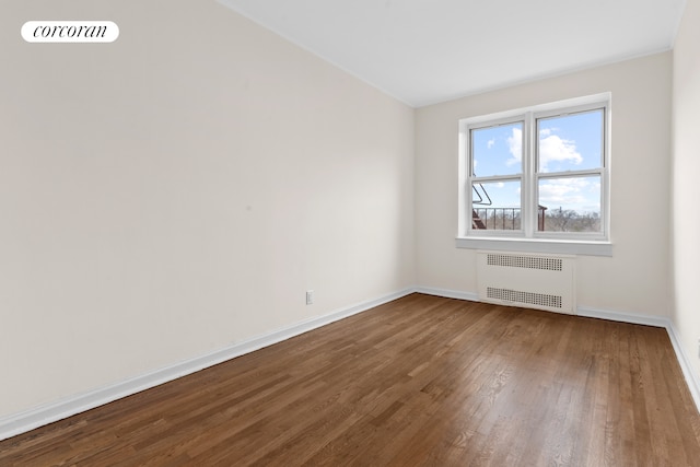 empty room with radiator heating unit, dark wood-type flooring, and baseboards