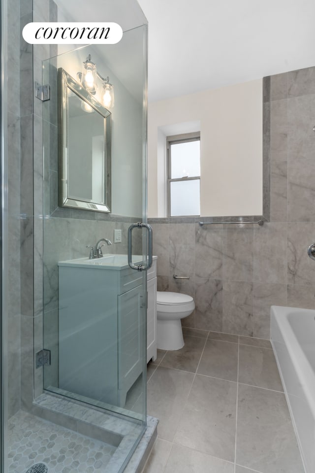 full bathroom with tile walls, a stall shower, toilet, vanity, and tile patterned flooring