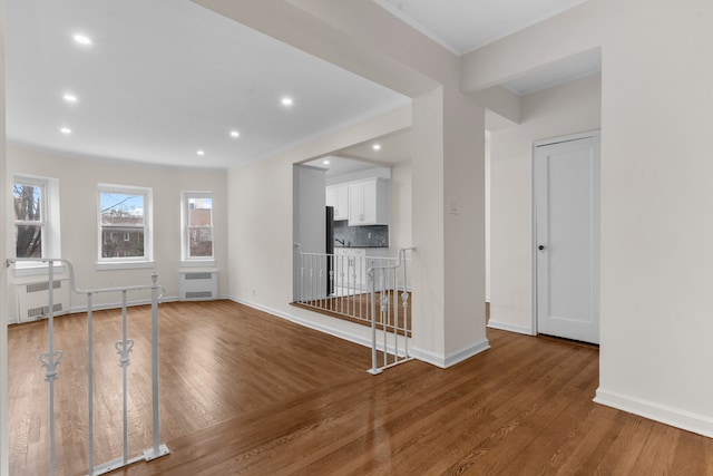 unfurnished living room featuring wood finished floors, baseboards, ornamental molding, recessed lighting, and radiator heating unit