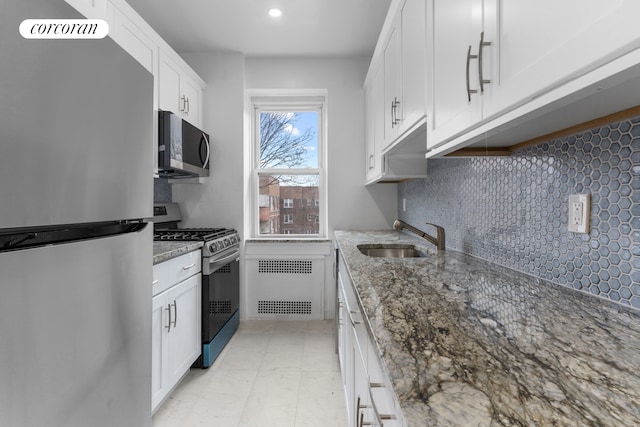kitchen featuring stainless steel appliances, radiator, a sink, backsplash, and white cabinets