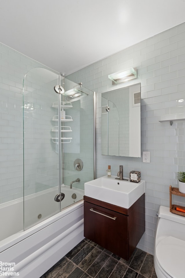 full bathroom with tile walls, toilet, vanity, and shower / bath combination with glass door
