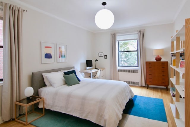 bedroom with radiator, light wood-type flooring, and crown molding