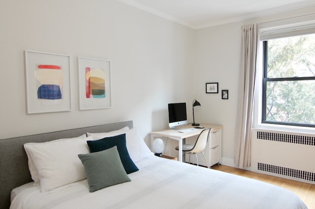 bedroom with radiator heating unit, wood finished floors, multiple windows, ornamental molding, and baseboards