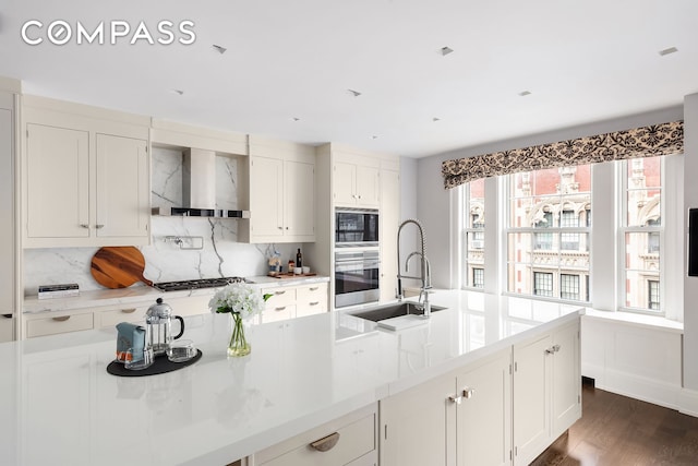40 E 66th St Unit 12B, New York City, NY 10065 - kitchen featuring stainless steel oven, wall chimney range hood, a sink, backsplash, and white cabinets