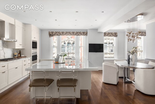 40 E 66th St Unit 12B, New York City, NY 10065 - kitchen featuring stainless steel appliances, dark wood-style flooring, wall chimney exhaust hood, and plenty of natural light