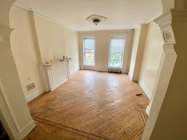 188 Mac Donough St, New York City, NY 11216 - empty room with ornamental molding, light wood-style flooring, arched walkways, radiator heating unit, and decorative columns