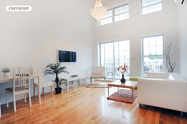 living area featuring a high ceiling, wood finished floors, a chandelier, and an AC wall unit