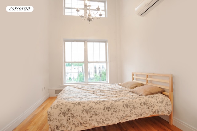 bedroom featuring an AC wall unit, multiple windows, baseboards, and wood finished floors