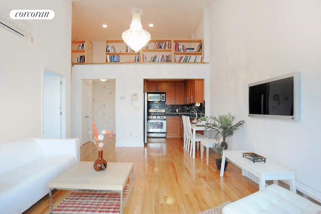 living area featuring light wood finished floors, a chandelier, an AC wall unit, a high ceiling, and recessed lighting