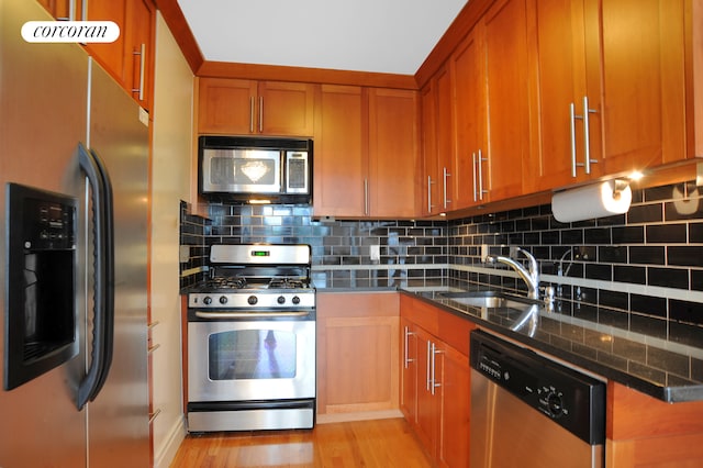 kitchen with stainless steel appliances, a sink, brown cabinets, light wood-type flooring, and tasteful backsplash