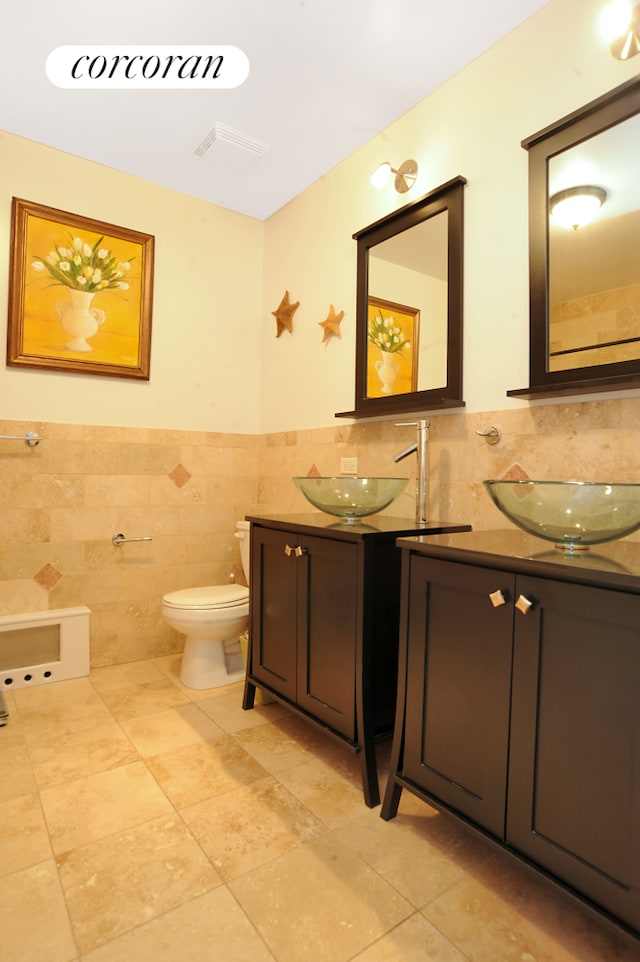 bathroom with tile walls, double vanity, tile patterned floors, toilet, and wainscoting