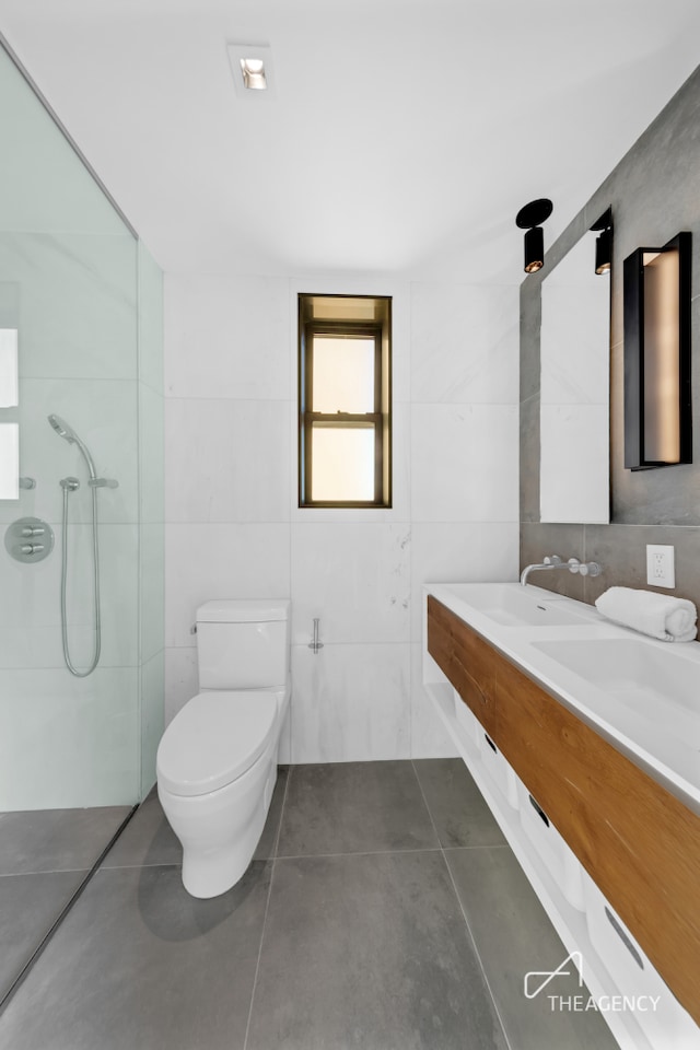 full bath with tile walls, tile patterned floors, a shower, double vanity, and toilet