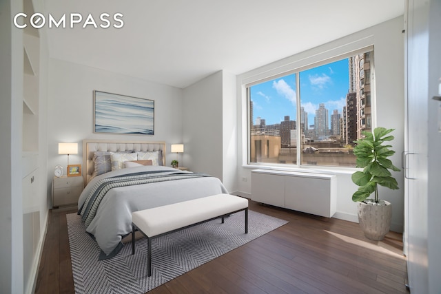 bedroom featuring dark wood-style floors, a view of skyline, and baseboards