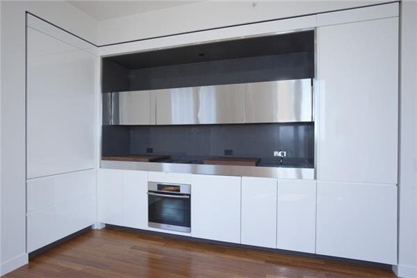 kitchen featuring stainless steel oven, white cabinets, dark wood-style floors, and backsplash