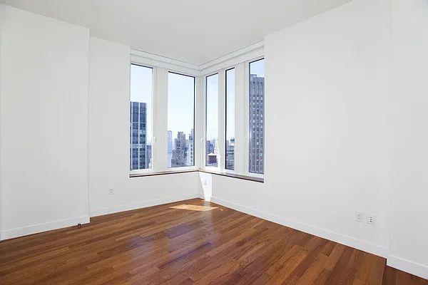 unfurnished room featuring healthy amount of natural light, dark wood-type flooring, baseboards, and a view of city