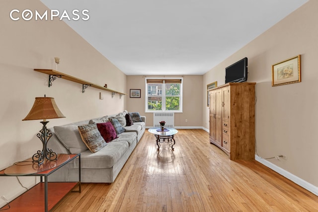 living area with radiator heating unit, light wood-type flooring, and baseboards