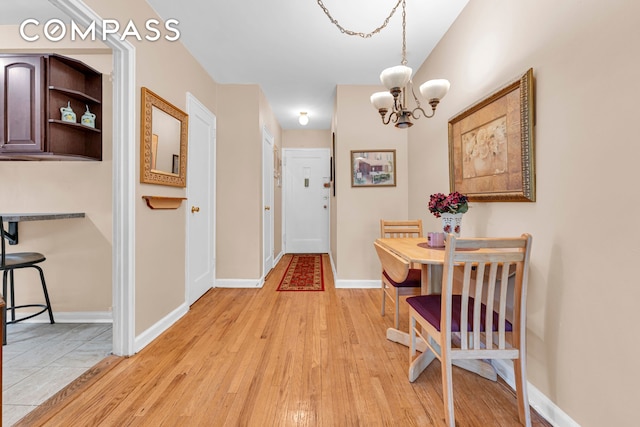 hall featuring a chandelier, light wood finished floors, and baseboards