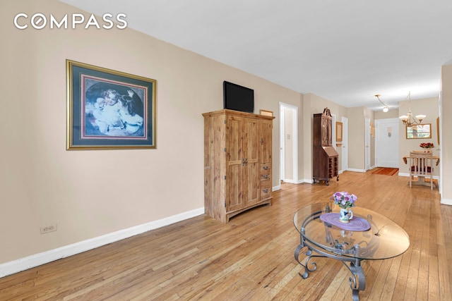 living room with light wood-style flooring, a chandelier, and baseboards