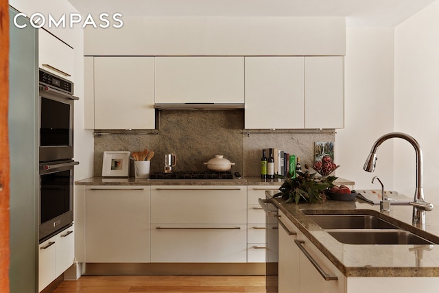 kitchen featuring a sink, stainless steel appliances, light wood-type flooring, and backsplash