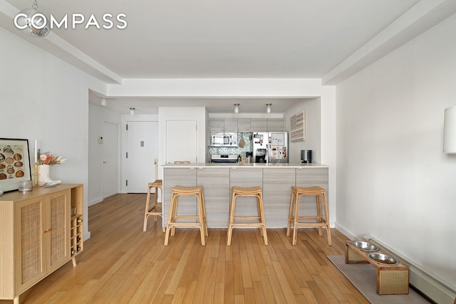 91-16 Shore Front Pkwy Unit 2F, New York City, NY 11693 - kitchen featuring stainless steel appliances, a peninsula, a kitchen breakfast bar, light wood-style floors, and light countertops
