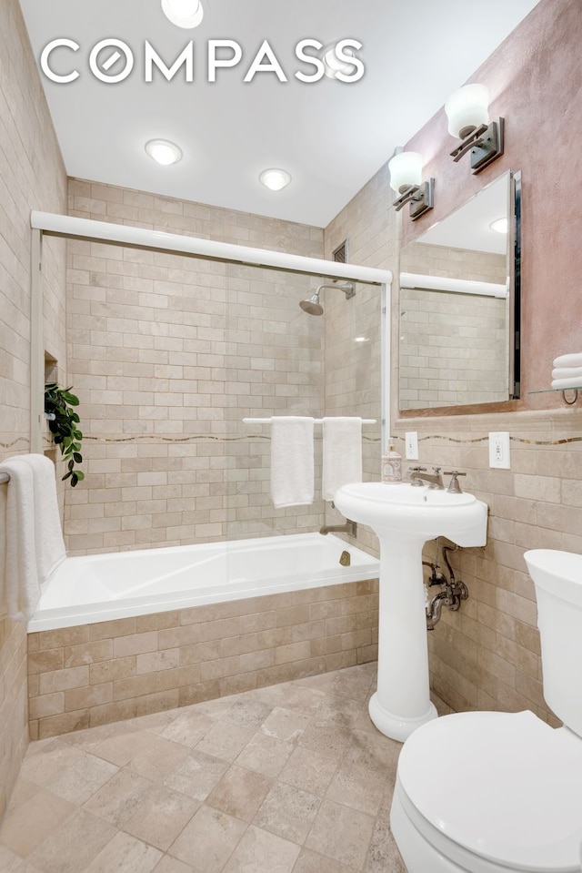 full bath featuring toilet, tiled shower / bath combo, and tile walls