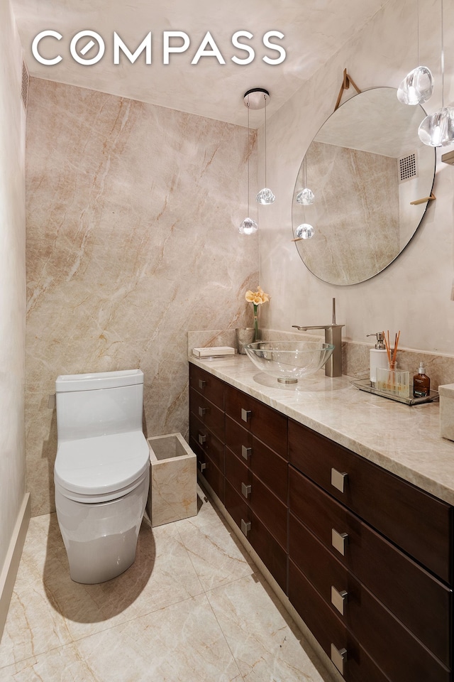 bathroom featuring toilet, vanity, marble finish floors, and tile walls