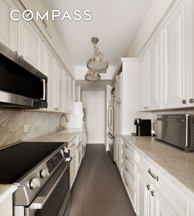 kitchen featuring appliances with stainless steel finishes, dark tile patterned floors, white cabinetry, backsplash, and a sink