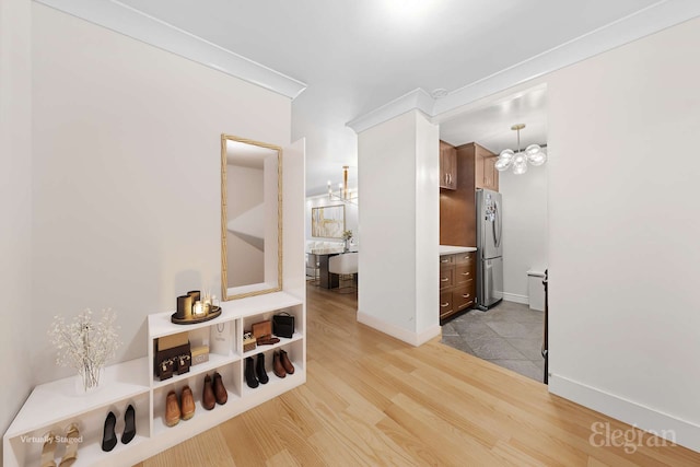 hall featuring light wood finished floors, baseboards, and a chandelier