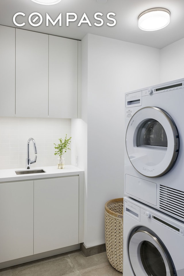 washroom featuring stacked washer / dryer, cabinet space, light tile patterned floors, and baseboards