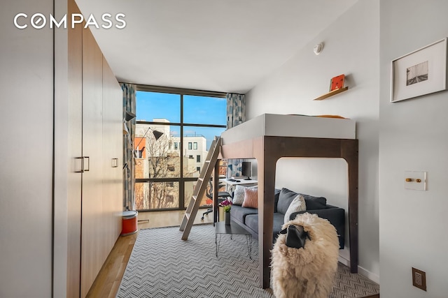 bedroom with expansive windows, wood finished floors, and baseboards