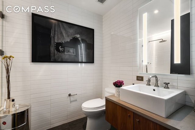 bathroom with tile walls, toilet, a shower, vanity, and tile patterned floors