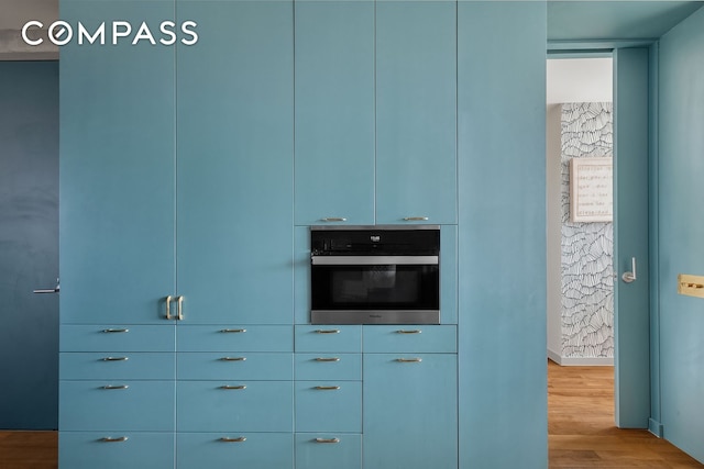 detailed view of wall oven, wood finished floors, modern cabinets, and baseboards
