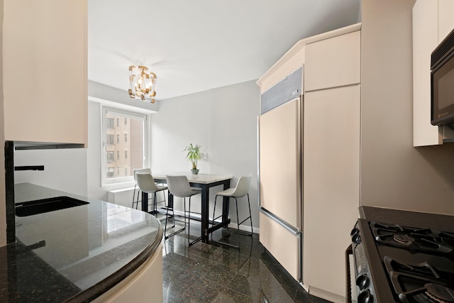 kitchen featuring built in fridge, granite tiled floors, gas range, a chandelier, and dark stone countertops