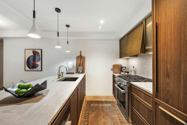 kitchen featuring high end stove, a sink, light countertops, light wood-style flooring, and hanging light fixtures